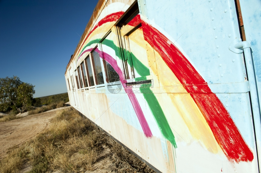 沙漠中的旧火车厢上面画着彩虹运输威尔士一种图片