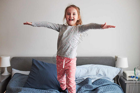 跳跃孩子面孔快乐的小玩女孩得开心做傻笑的脸在床上跳早卧室家图片