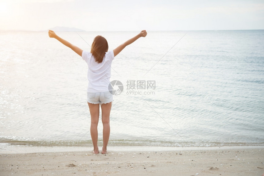 在海滩上赤脚放轻松的节日中站在空伸着双臂的年轻女子后背放松假期图片