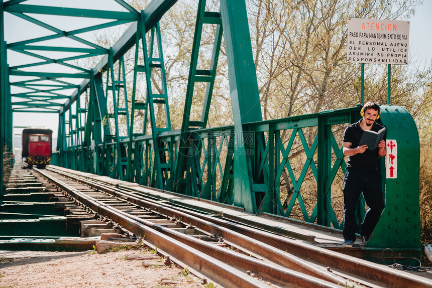 世界年轻建筑工人坐在一旁看本关于旧钢铁路桥的书坐着火车建造图片
