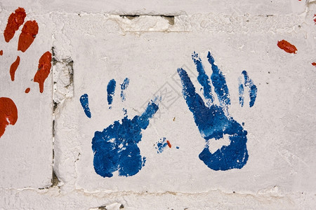 丰富多彩的白混凝土墙上一对蓝色和红手印在南非的一个乡镇学龄前隔离墙上展示出色彩多的外表图纸画背景