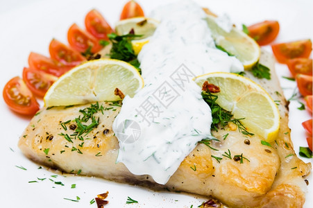 美食白盘上加蔬菜和奶油酱的烤鱼海鲜晚餐图片