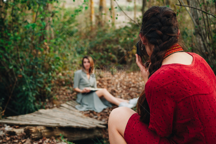 连衣裙女年轻一对身着洋装的年轻女子在森林里阅读一本书并用旧相机拍照年轻的图片