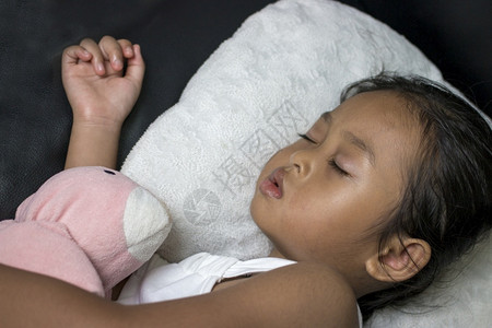 泰迪熊睡眠可爱的小女孩睡在黑沙发上和最喜欢的玩具睡觉白种人图片