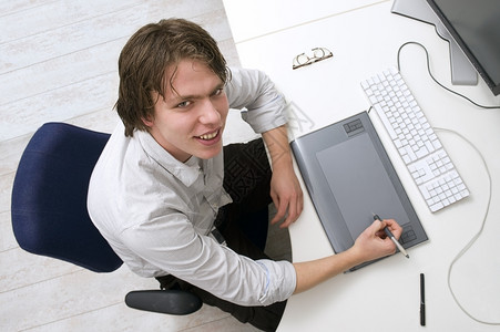 桌子白种人坐在办公桌后面有键盘图形平板和监视器的办公室内快乐图片