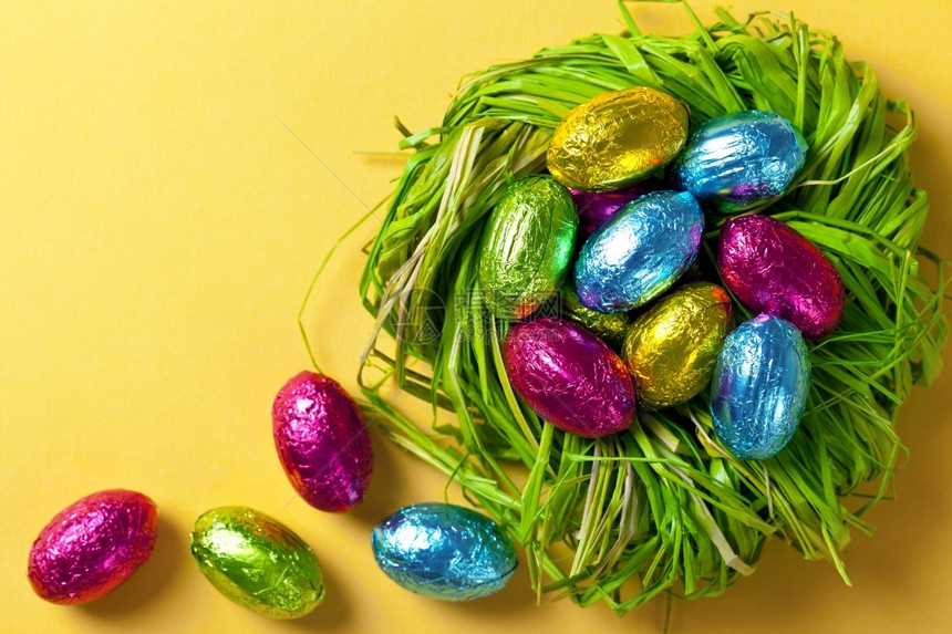 颜色彩复活节蛋在绿巢中黄纸背景上的假日组合物顶视图丰富多彩的蓝色图片