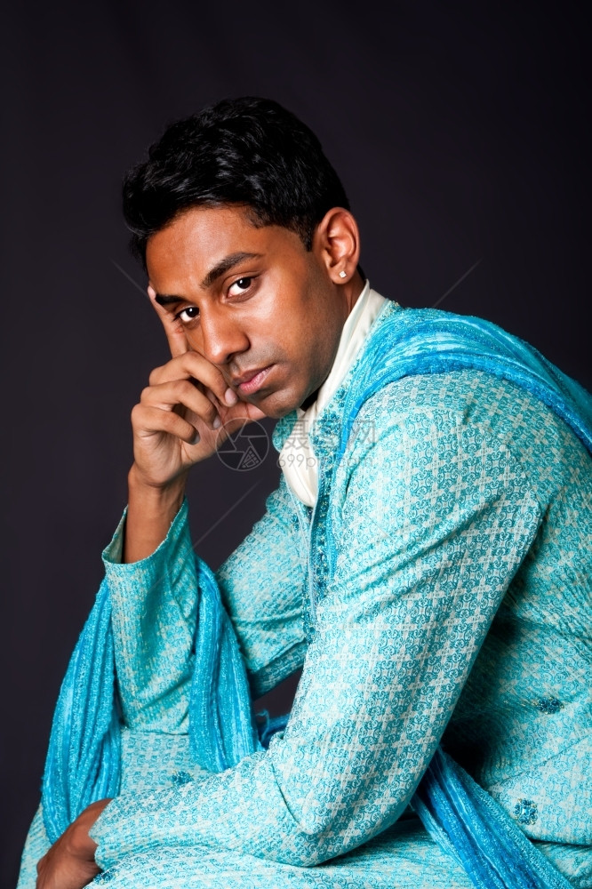 一位印度青年的美丽面容他戴着耳环身蓝色DhotiPortrait长相英俊的Desi男坐着思考与世隔绝巴基斯坦多提思维图片