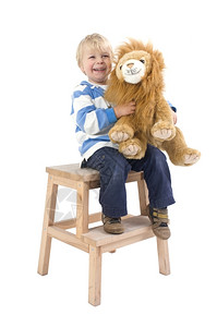 耍狮子小男孩一种个3岁的男孩坐在凳子上拿着一只玩具狮子微笑着老的木头背景
