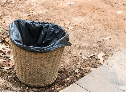 包木头正面Wicker篮子垃圾桶在农村住宅前的地面上背景图片