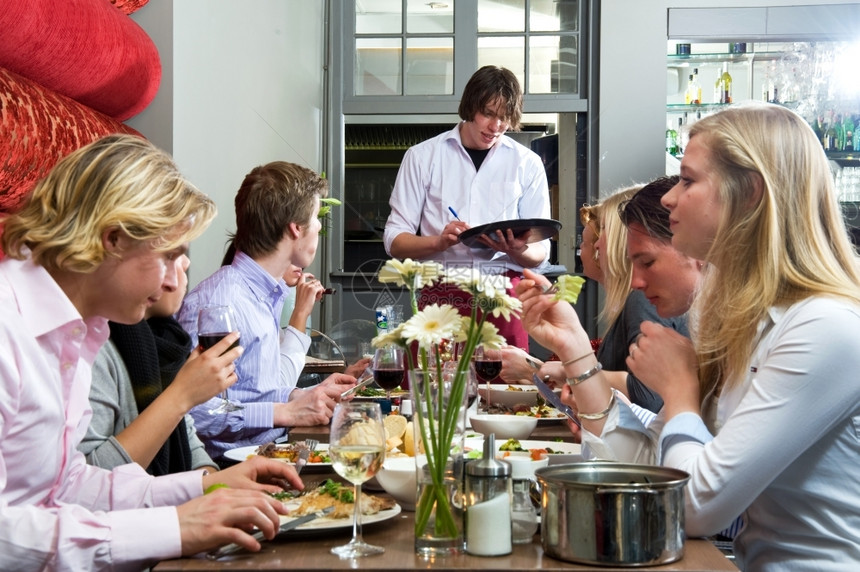 友好舒适时髦的服务员接受一群在餐厅吃饭的客人命令请进图片