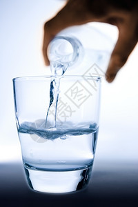 用手把水从瓶子倒到半杯玻璃背光浇注图片