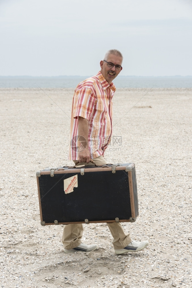 水旅游在海滩上行走的旧古老男子用手提箱优质的图片