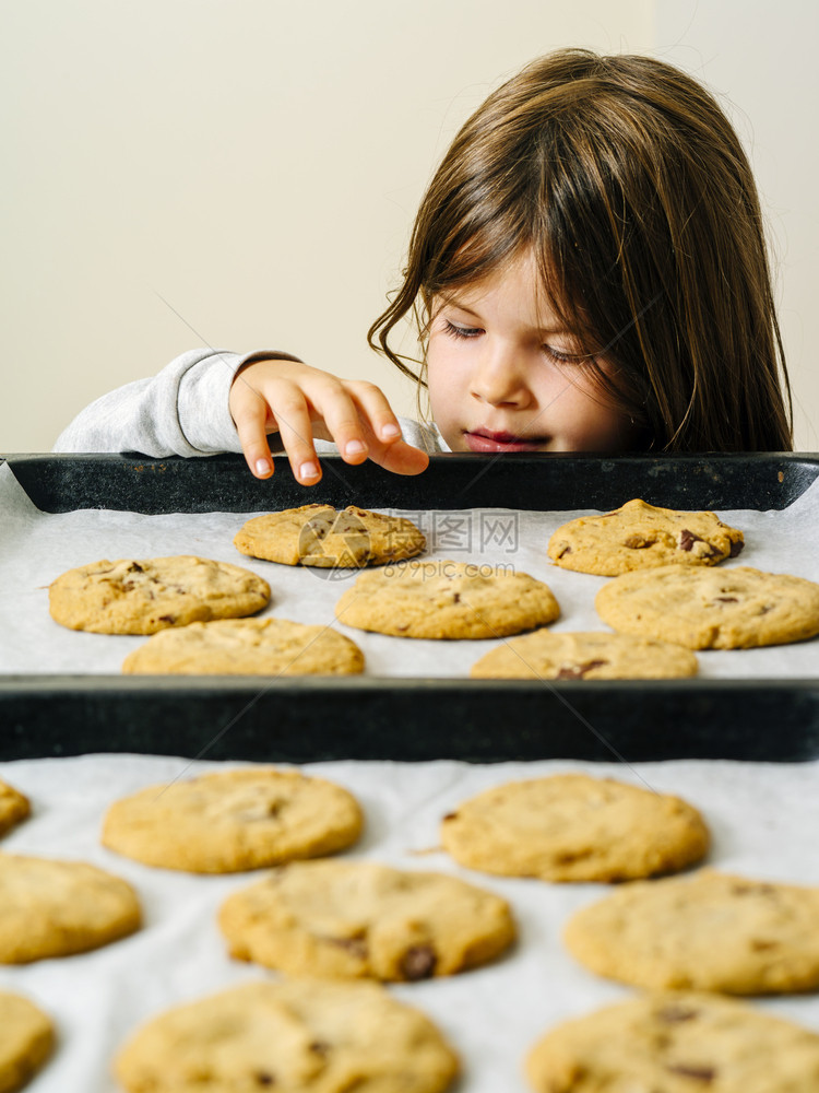 烘烤的一个年轻女孩从烘烤盘上抢取一个温暖巧克力饼干的照片孩子厨房图片