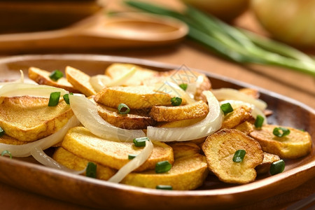 红薯切片有油炸洋葱和对木制板上火腿的炒洋葱和粉脆的脂肪土豆图片