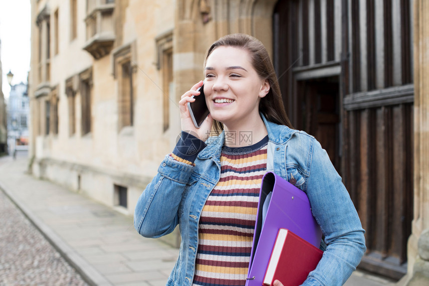 自信的女学生在大楼外的移动电话上交谈校外建筑部的女图片