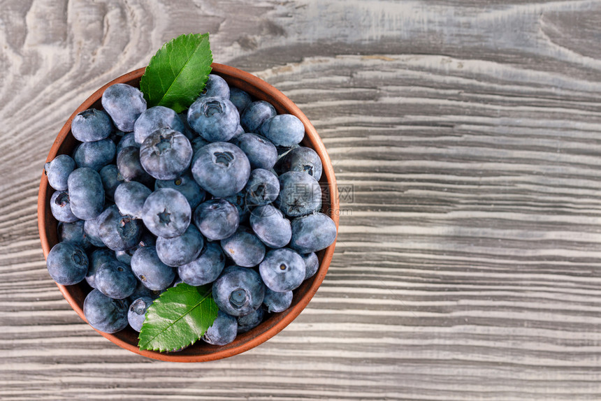 蓝莓和棕色粘土碗中的叶子木制背景从蓝莓上方看木制背景的泥土碗中叶子一种饮食物图片