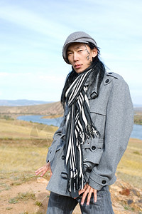 草原成吉思汗身着灰色大衣帽子和条纹黑白围巾的年轻亚洲人他脸上的痕迹是古蒙语中他的名字Chinghis古老的图片