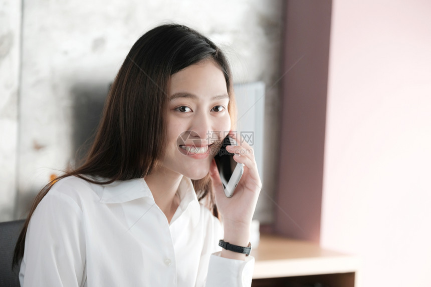 美丽的聪明年轻亚洲女商人讲智能电话带着快乐的情绪微笑在家工作办公室临时生活方式概念在办公室工作技术图片