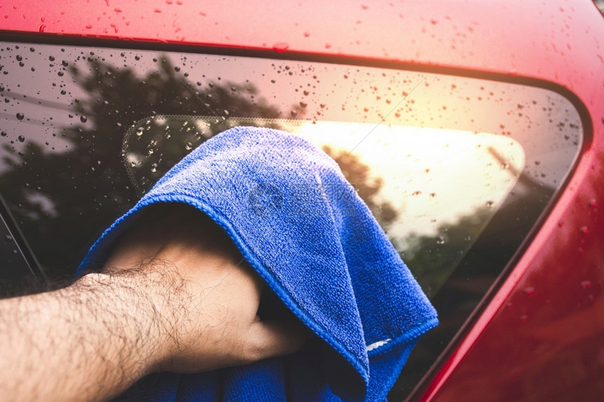 身体阳光运输人的手正在用蓝色微纤维布擦洗汽车玻璃杯上的水滴子图片