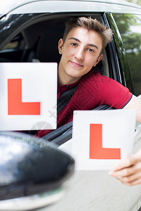 驾驶微笑青少年男孩驾车通过考试前持有学习者平台的肖像倾斜图片