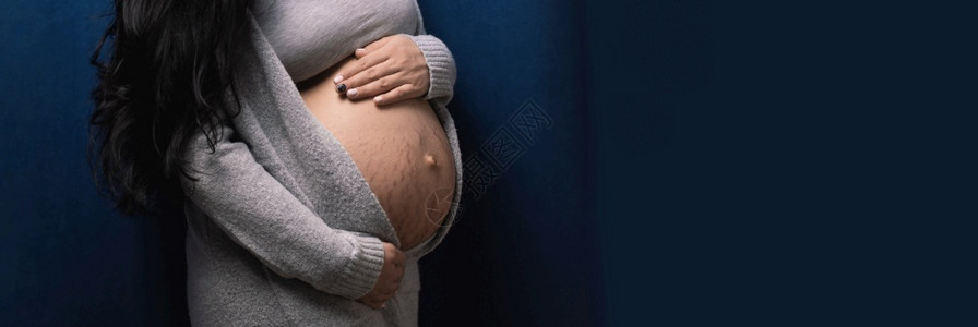 年轻的快乐孕妇在蓝色背景婴儿等待概念下抚摸肚子的婴儿等候概念女孩图片