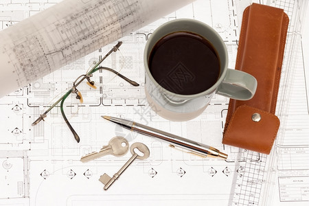 卷配有钥匙和咖啡的建筑计划草图蓝图片