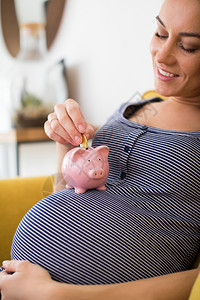保持硬币推杆护士室的孕妇将钱放进小猪银行在胃部休息图片