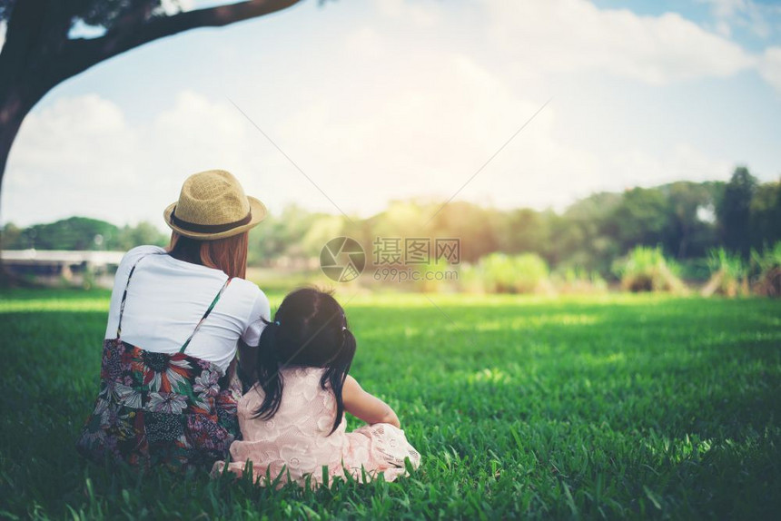 年轻母亲和女儿坐在公园绿草地上放松在公园里休息女士孩坐着图片