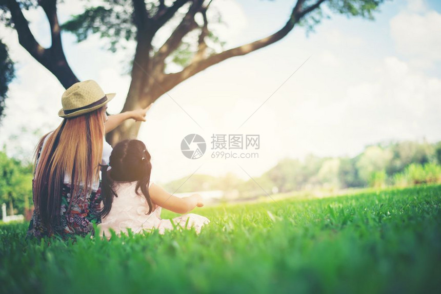 年轻母亲和女儿坐在公园绿草地上放松在公园里休息女娱乐婴儿图片