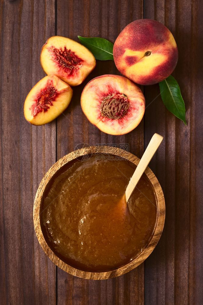 木碗中的桃子果酱或冻边上有新鲜成熟的桃子水果用天然轻光桃子酱或果汁在黑木头上拍摄了相片勺子或者自然图片