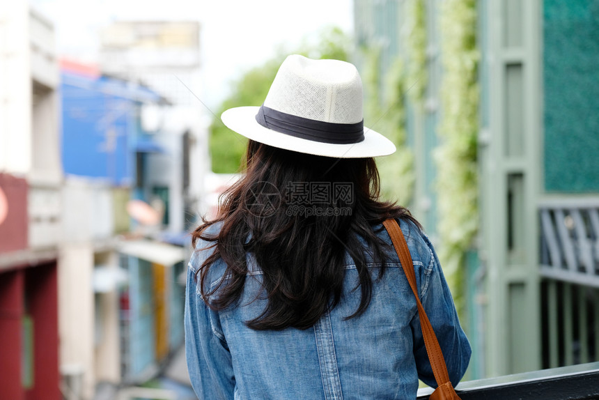 博主与城市户外背景站在一起的女旅行者背面临时生活者旅行博客帽子随意的图片