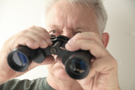一个年长的男人拿着一副旧的双筒望远镜水平的脸警报图片