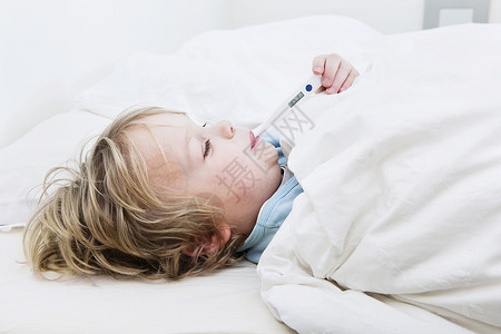 嘴流感年轻的在家生病年轻男孩在床上用温度计测量他的体温图片