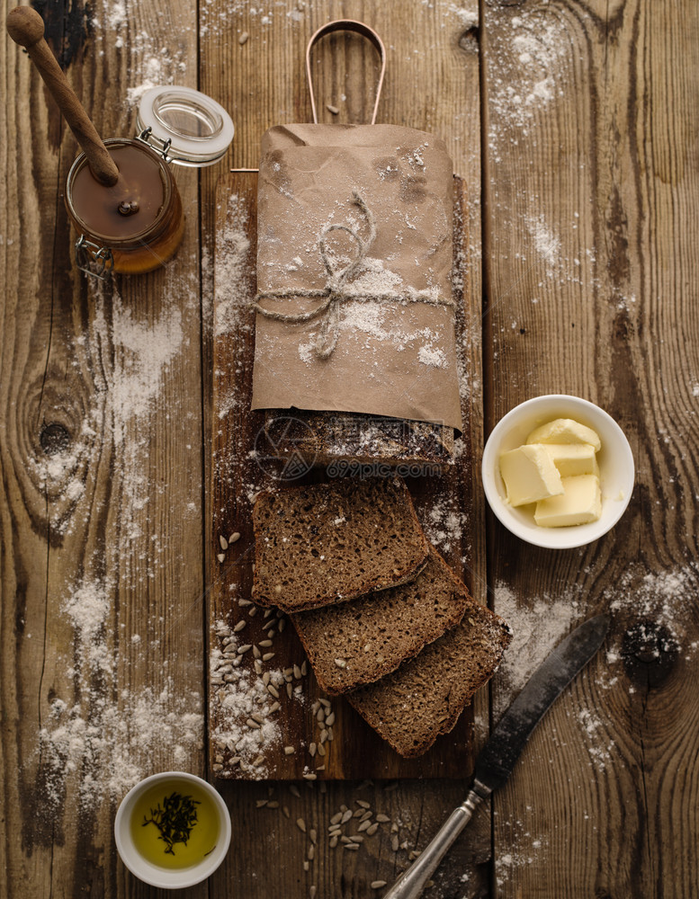 蜜糖健康用黄油和蜂蜜在木背景上切成自制黑麦面包一种图片