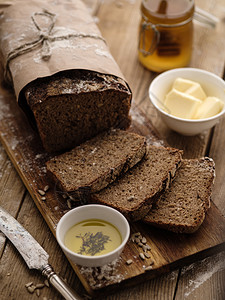用黄油和蜂蜜在木背景上切成自制黑麦面包木的桌子店图片