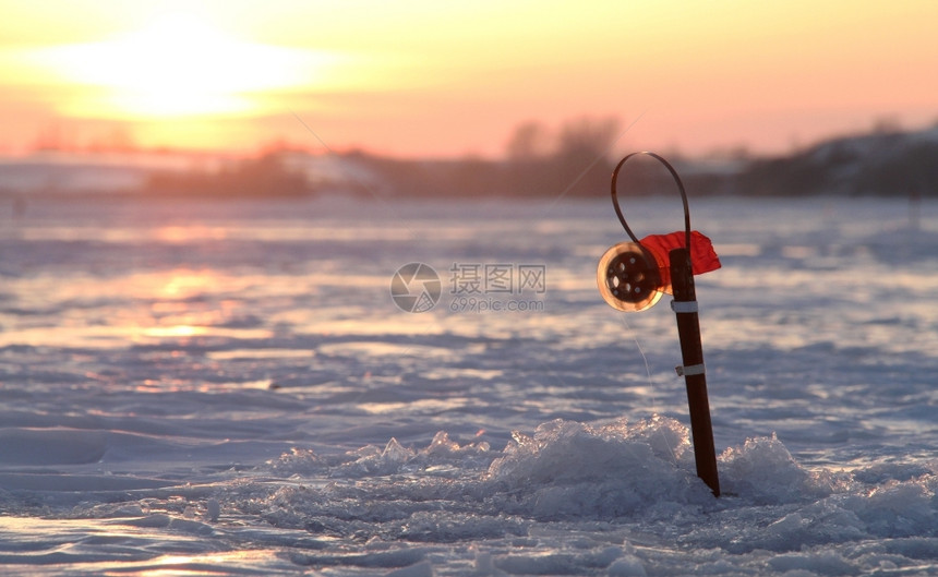 在日落时湖边冰洞中捕冬季鱼的渔船棒为了寒冷的闲暇图片
