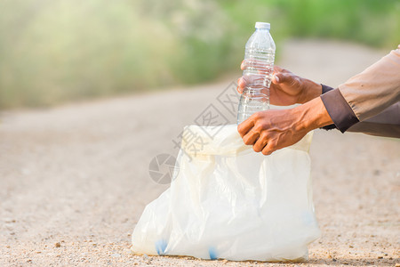 男士目的包曼诺斯手正在把塑料瓶捡到垃圾袋里生态概念图片