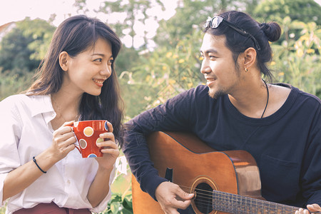 在公园里弹吉他歌唱的亚洲年轻男人和女士玩肖像图片