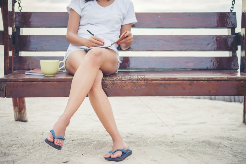 户外年轻美女在沙滩上放松时坐在长椅上用笔记本写字杂志手图片