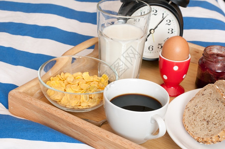 Bed早餐面包果咖啡煮蛋牛奶玉米片和闹钟床枕头浪漫的图片