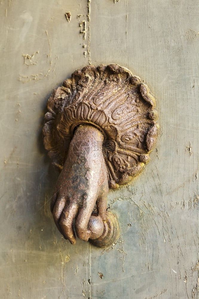 球夹具一只神秘的手从门外伸出来握着一个敲门机这生锈的装饰固定置在意大利奥维托的一扇门上来了图片