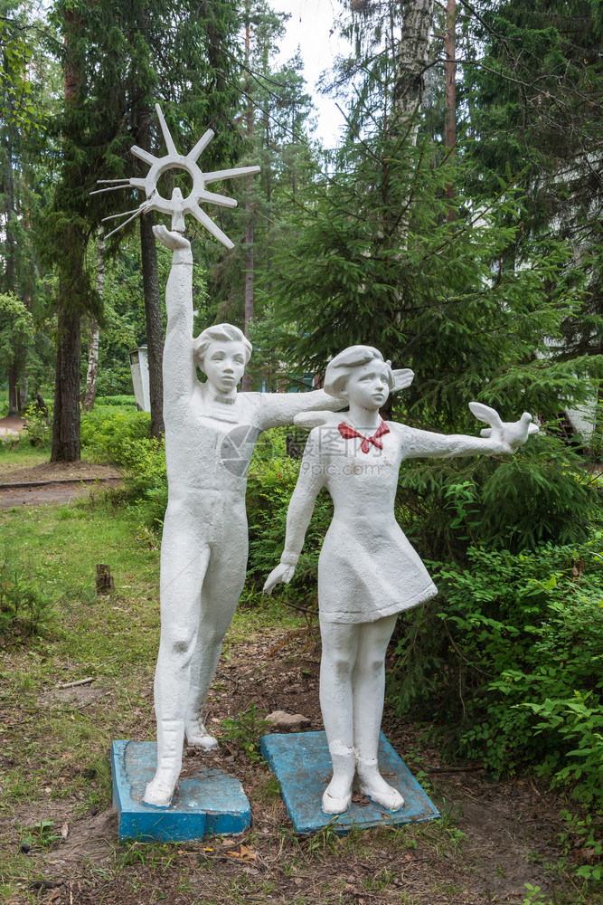 在俄罗斯绿树背景下一个男孩和女的雕塑与苏维埃时代一只鸽子从苏维埃时代来到俄罗斯青年树木老的图片