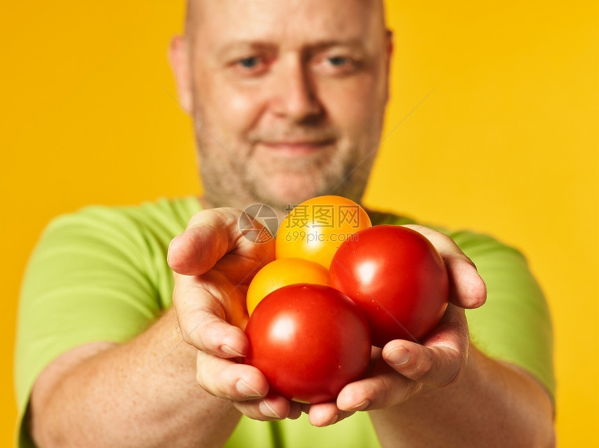 健康中年人和手头新鲜熟西红柿黄色背景老化蔬菜图片