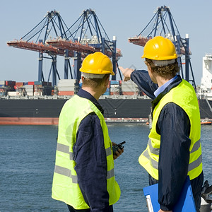码头工人在职的讨论中两艘停靠船指出一艘大型集装箱船舶的卸货作业人们图片