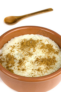 健康勺子奶油的土制大米在陶瓷碗和白隔绝的木勺中加牛奶和肉桂图片