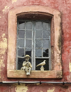 红色窗格建造法国在普罗旺斯的一个小镇上男孩在吹笛子和鸽时坐在窗帘上的雕像红色背景