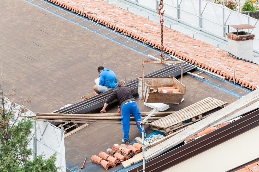 建筑屋顶大楼翻修的工人建筑房顶改造中的工人屋顶男艺图片