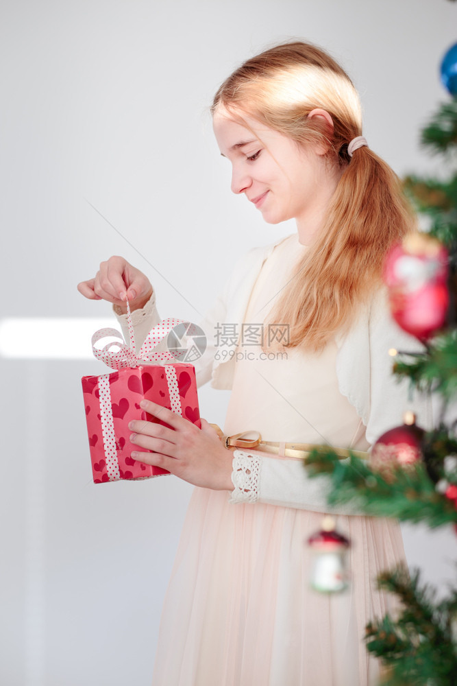 粉色的圣诞节时候孩子快乐女在树后拆开圣诞礼物站立在树后面图片