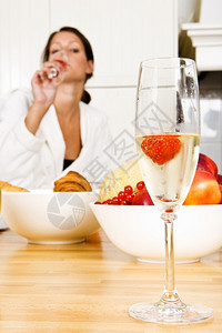 隐隐约约厨房木头香槟笛子里面有草莓和一个漂亮的黑发女人在背景中昏暗地代表着一个香槟早餐在情人节的晚宴上一种背景