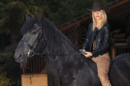 一个美丽的金发女孩骑在黑马上全套服装年轻的快乐图片